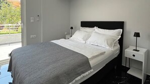 A modern bedroom with a large bed, white bedding, a grey throw blanket, and a nightstand with a lamp. - 4 minutes by car from the beach new modern apartment in Rhodes town (Rodos)