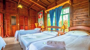 A wooden cabin with four beds, a large window with blue curtains, and a painting on the wall. - Finca Hotel El Ocaso Quimbaya (Quindío)