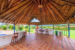 A covered outdoor area with a tiled floor, wooden furniture, and a view of a lush landscape.