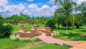 A circular brick patio with a central fire feature, surrounded by lush greenery and palm trees. - Finca Hotel El Ocaso Quimbaya (Quindío)