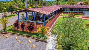 A two-story building with a red-tiled roof, a covered outdoor seating area, and a well-maintained garden with palm trees and shrubs. - Finca Hotel El Ocaso Quimbaya (Quindío)
