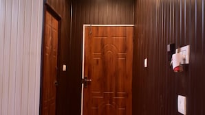 Habitación de hotel con paredes y puerta de madera, una cama con manta blanca, una mesita pequeña y un aplique de pared.