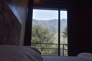 A bedroom with a large window offering a view of a mountainous landscape.