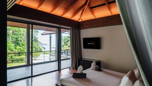 A modern hotel room with a large bed, a flat-screen TV, and a balcony with a view of greenery and a building. - Princess Maria - 6BR seaview villa in guarded estate, 250m from Kata Noi Beach (Tambon Karon)