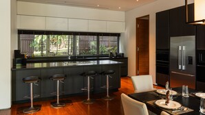 A modern kitchen with a central island, bar stools, a dining table set for four, and a large refrigerator. - Princess Maria - 6BR seaview villa in guarded estate, 250m from Kata Noi Beach (Tambon Karon)