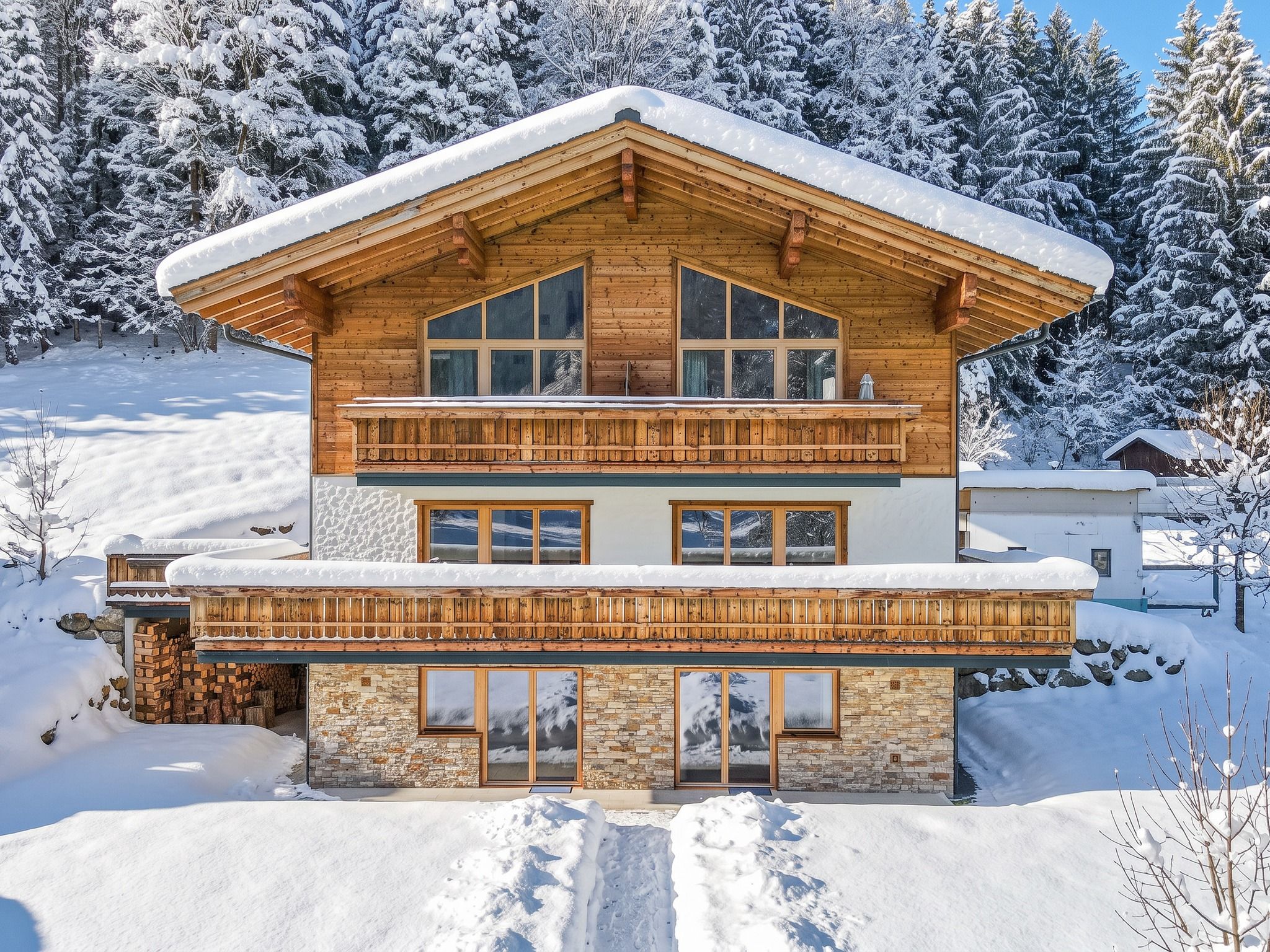 Un chalet en bois à deux étages, doté d’un balcon, de fondations en pierre et de grandes fenêtres.