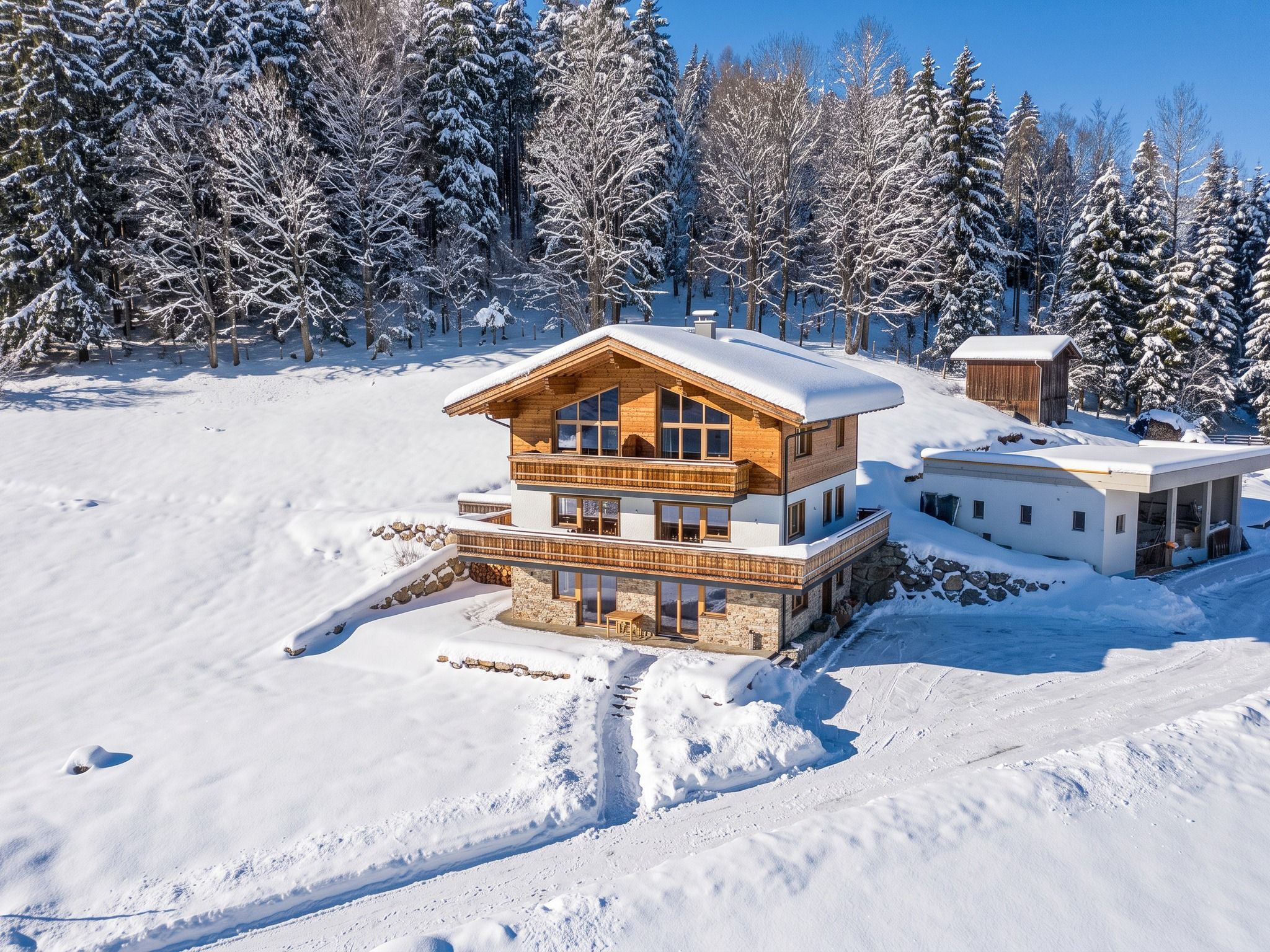 A wooden chalet with a balcony, set in a snowy landscape with trees.