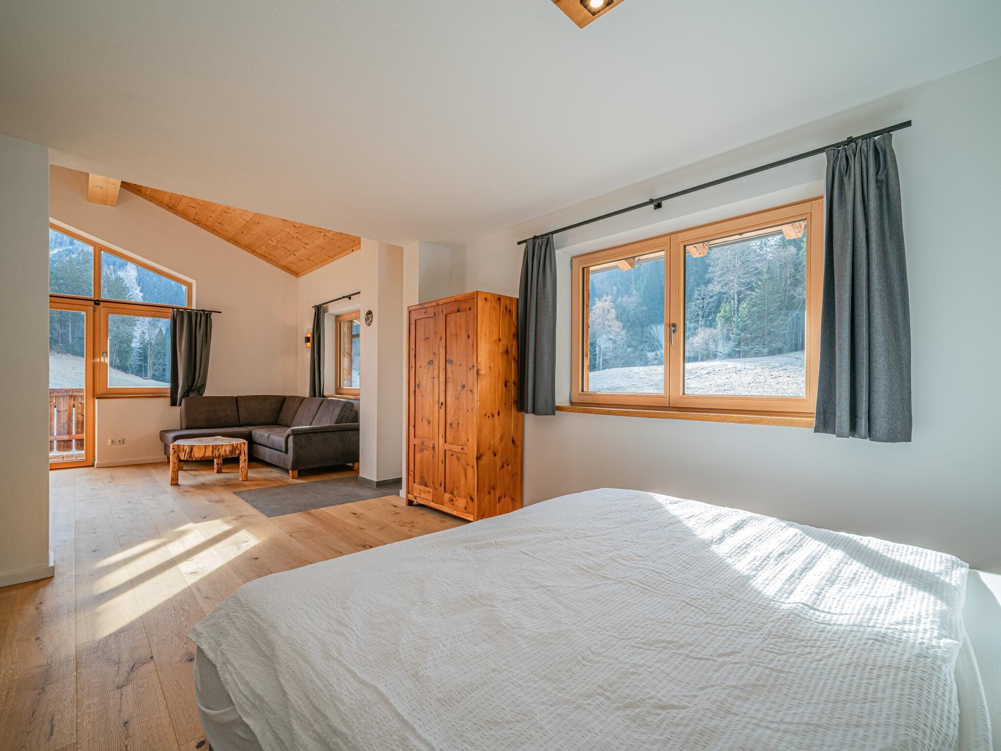 A bedroom with a large bed, a wooden wardrobe, a sofa, and a window with curtains.