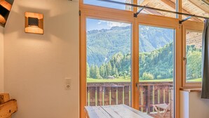 A wooden table and bench in a room with large windows overlooking a forested mountain landscape. - Cosy holiday flat with mountain views (Vorderkrimml)