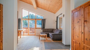 A spacious living room with a wooden ceiling, large windows, a gray sofa, and a wooden cabinet. - Cosy holiday flat with mountain views (Vorderkrimml)