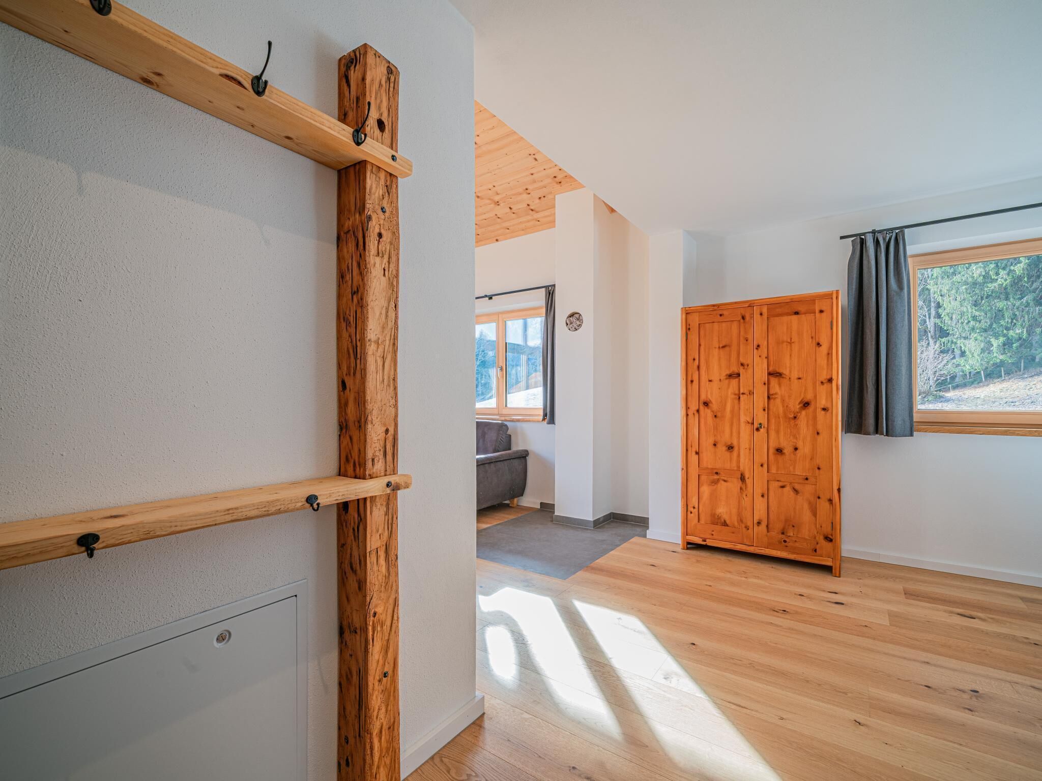 Un interior moderno con vigas de madera, una puerta grande de madera y vistas a un paisaje montañoso a través de una ventana.
