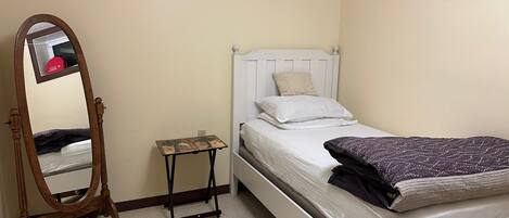 A bedroom with a single bed, a small table, a mirror, and a wardrobe.