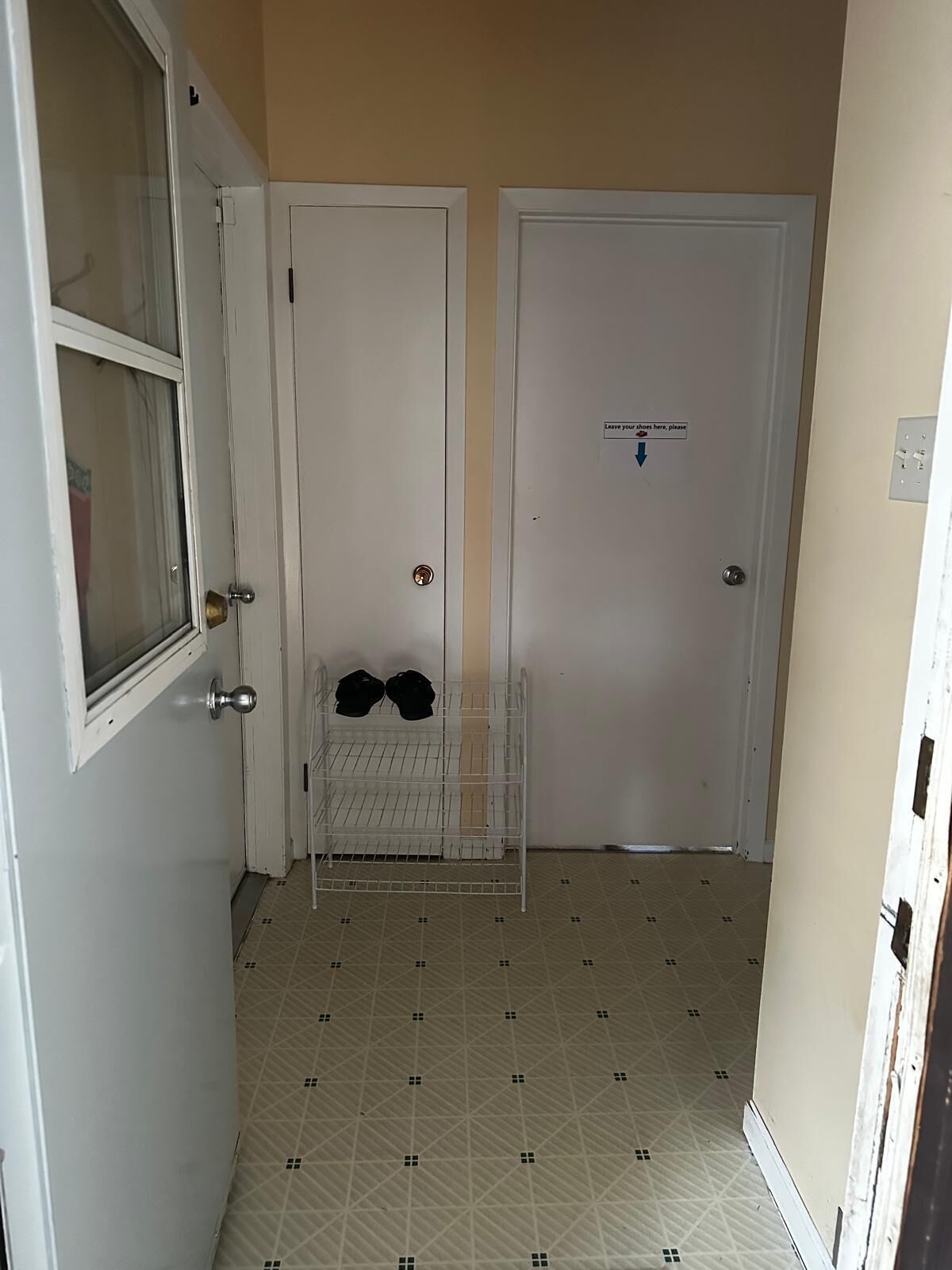 Un pasillo con dos puertas blancas, una con un letrero que indica quitarse los zapatos, y un perchero con sombreros.