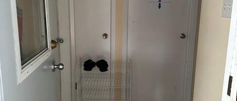 Un pasillo con dos puertas blancas, una con un letrero que indica quitarse los zapatos, y un perchero con sombreros.
