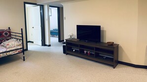 A bedroom with a bed, a TV on a stand, and a door leading to another room. - 1500 Sqft Entire Basement Private Suite - Extra Spacious & Cozy (Saskatoon)
