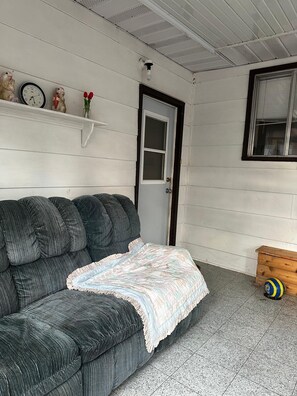 A room with a dark green sofa, a white door, a small wooden chest, and a wall-mounted shelf with a clock and figurines.