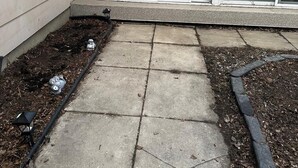 A patio area with a concrete floor, a small garden bed with mulch, and a metal pipe. - 1500 Sqft Entire Basement Private Suite - Extra Spacious & Cozy (Saskatoon)