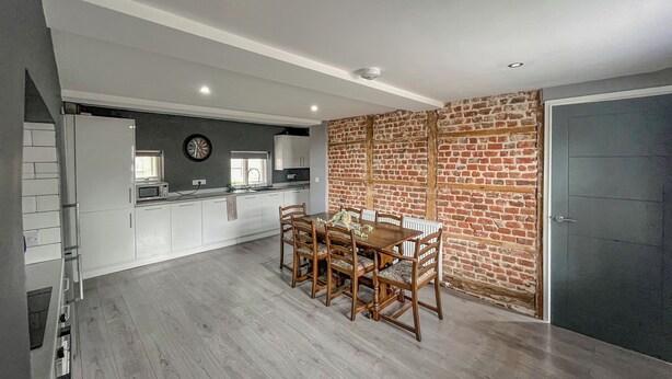 Una cucina moderna con mobili bianchi, una zona pranzo con tavolo e sedie in legno e un muro in mattoni.