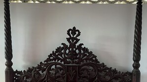 A four-poster bed with a dark wooden headboard featuring intricate carvings.