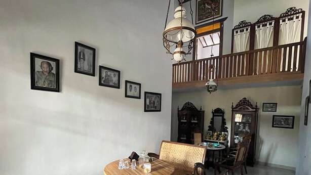A dining area with a round wooden table and chairs, a hanging light fixture, and framed pictures on the walls.