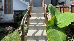 A staircase leading to a house with a grey exterior, a wooden handrail, and a window with a curtain.