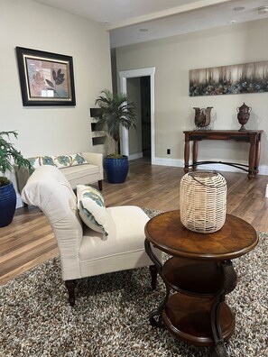 Un salon avec un fauteuil beige, une table basse ronde en bois, un grand panier en osier, un palmier en pot et un tableau accroché au mur.