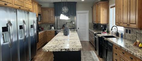 A modern kitchen with wooden cabinets, stainless steel appliances, and a granite countertop island.