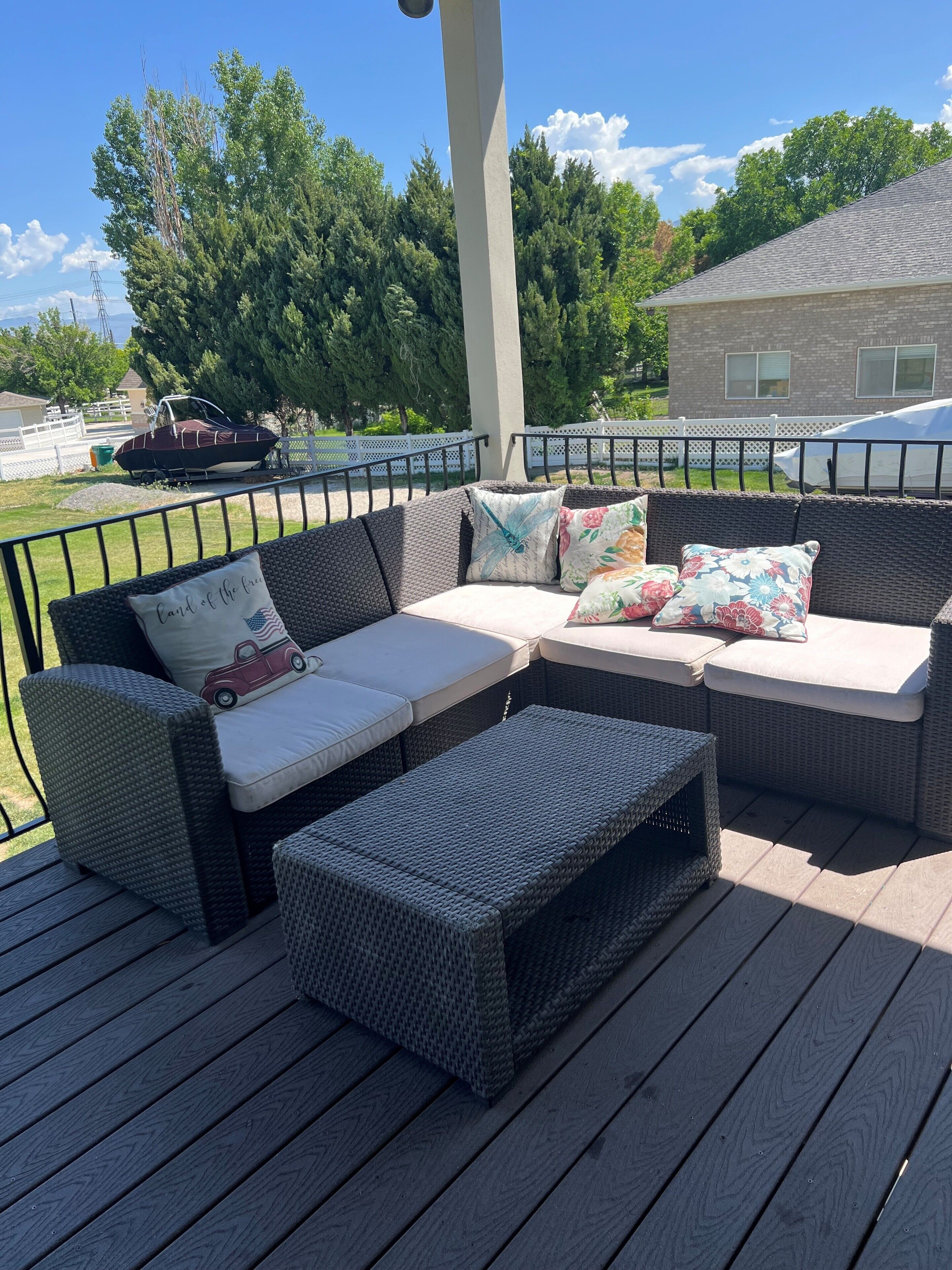 A covered outdoor seating area with wicker furniture, including a sofa and ottoman, and a boat in the background.