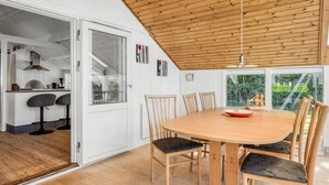 Una cocina moderna con armarios blancos, techo de madera y comedor con mesa y sillas de madera.
