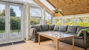 Una habitación soleada con techo de madera, un sofá gris y una mesa de madera.