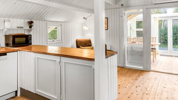 Cocina con armarios blancos, encimera de madera y microondas integrado. Hay una ventana y una puerta que dan a un espacio exterior con terraza de madera.
