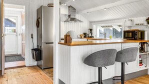 Una cocina moderna con armarios blancos, encimera de madera, refrigerador de acero inoxidable, microondas y dos taburetes de bar.