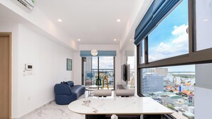 Un moderno salón con suelo de mármol, un sofá azul, una mesa de comedor con sillas, un televisor y un amplio ventanal con vistas a la ciudad.