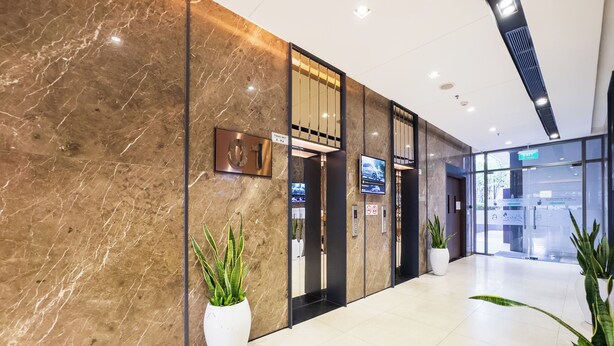 Un moderno vestíbulo de hotel con paredes de mármol, una recepción, ascensores y plantas en macetas.