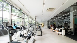 Un gimnasio con equipo de ejercicio, ventanas amplias y vistas a árboles fuera.