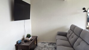 A living room with a flat-screen TV mounted on the wall, a dark wooden coffee table with a plant, a grey sofa, and a fluffy grey rug. - Cozy apartment near the GNP stadium (Ciudad de México)