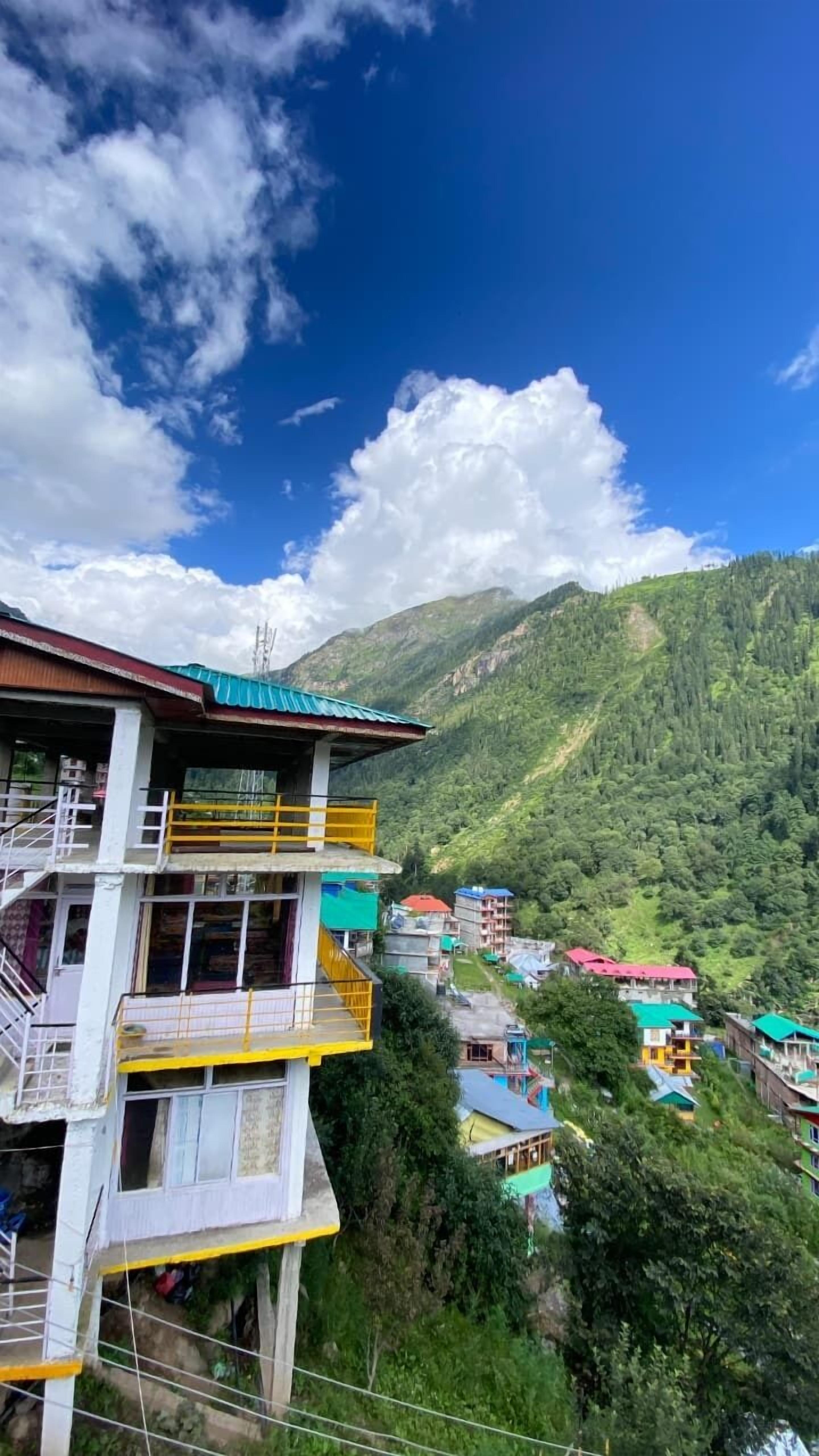 Un edificio de varios pisos con balcones, rodeado de exuberantes montañas verdes y un cielo azul despejado.