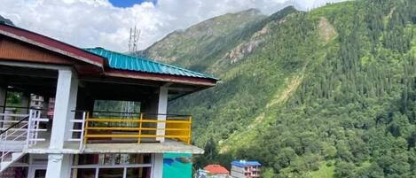 Un edificio de varios pisos con balcones, rodeado de exuberantes montañas verdes y un cielo azul despejado.