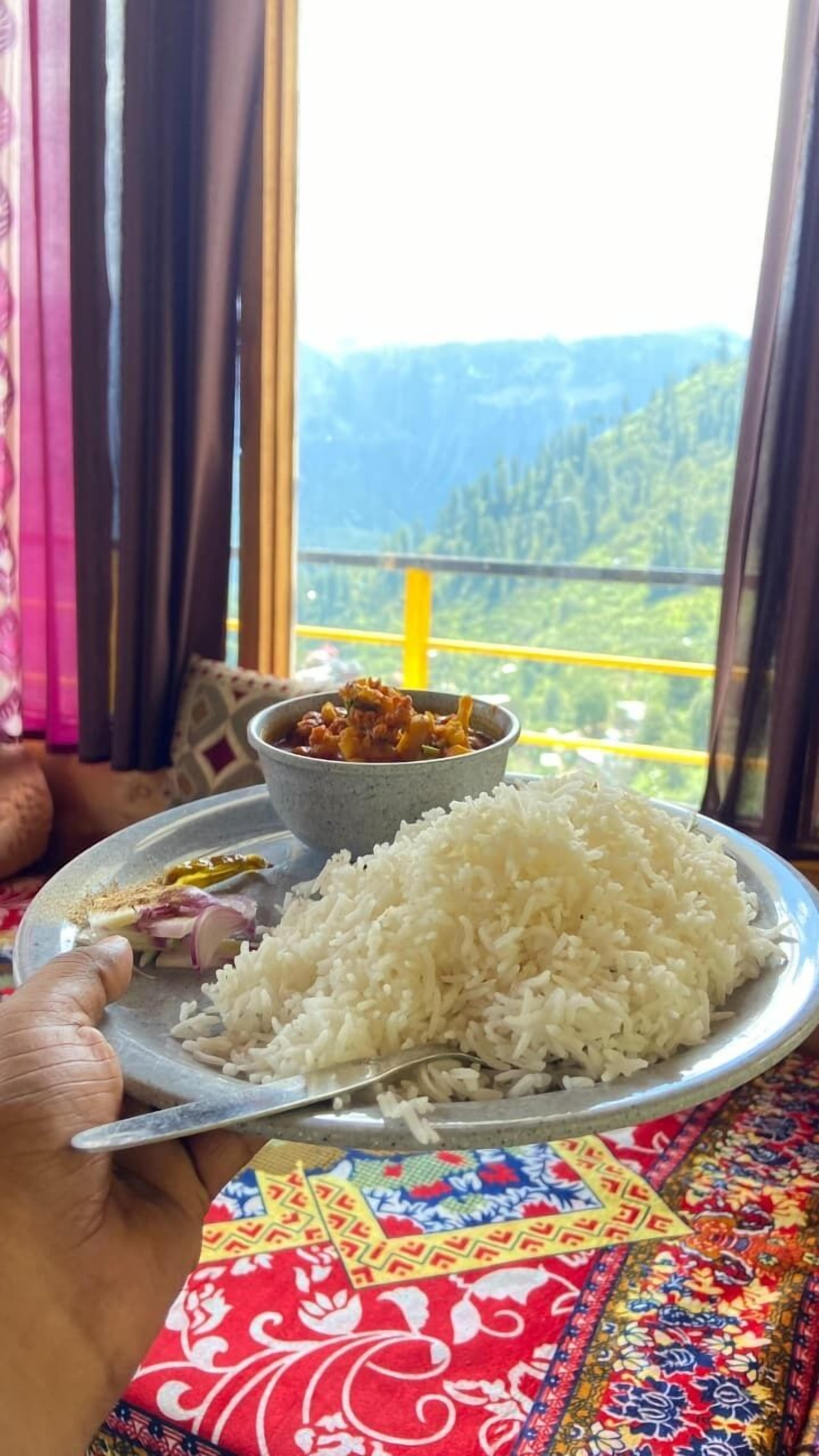 Un plato de arroz blanco y un cuenco de curry, sostenidos por una persona con mantel de estampado colorido.