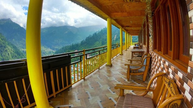 A covered balcony with wooden furniture and a view of a mountainous landscape.