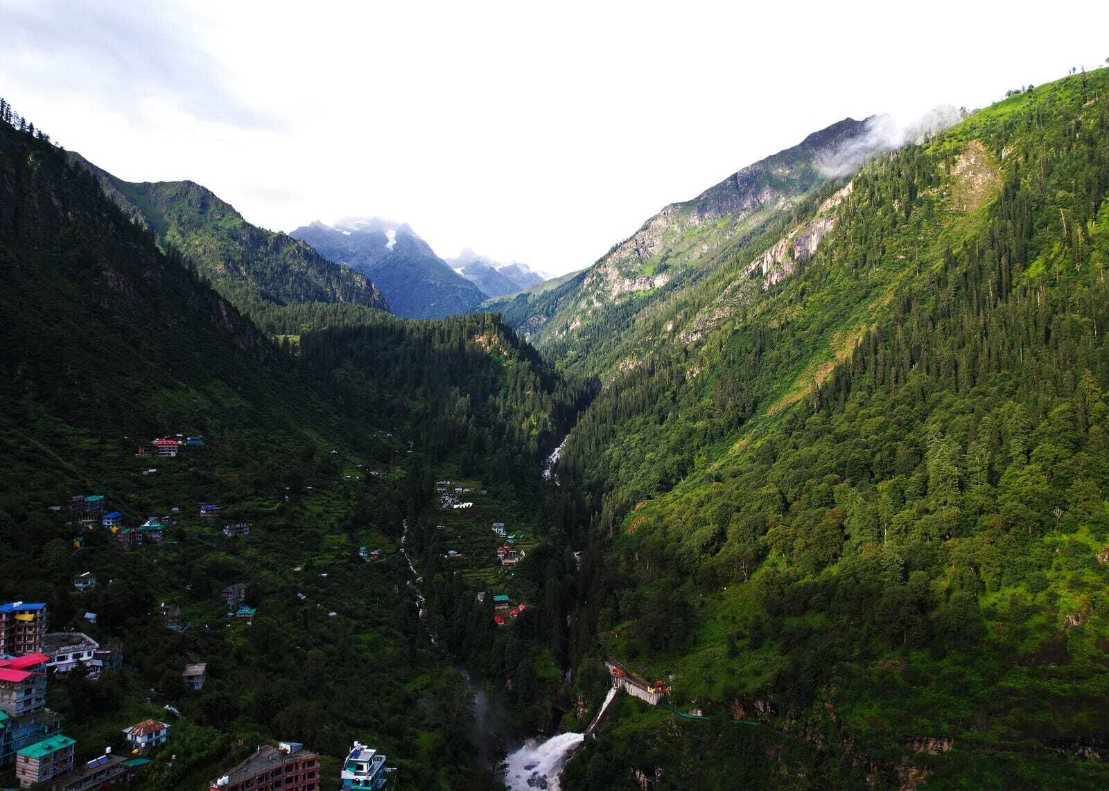 Een bergachtig landschap met een rivier die door een vallei stroomt, omgeven door dichte bossen en enkele verspreide gebouwen.
