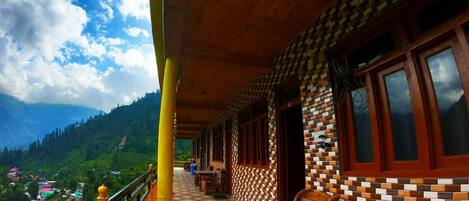 A covered balcony with a wooden ceiling, patterned walls, and a view of a mountainous landscape.