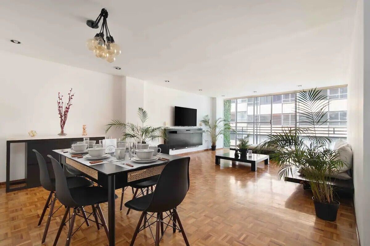 A modern living room with a dining area, a flat-screen TV, and large windows.