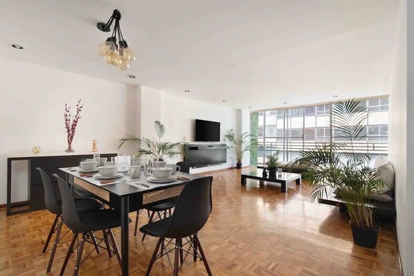 Un salon moderne comprenant un coin repas, un téléviseur à écran plat et de grandes fenêtres.