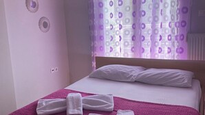 A bedroom with a bed, white pillows, a purple blanket, and two towels folded on the bed. - Epanomi apartments (Epanomi)