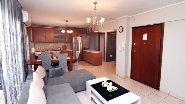 A modern living room with a grey sofa, a white coffee table, and a dining area with a wooden table and chairs. - Epanomi apartments (Epanomi)