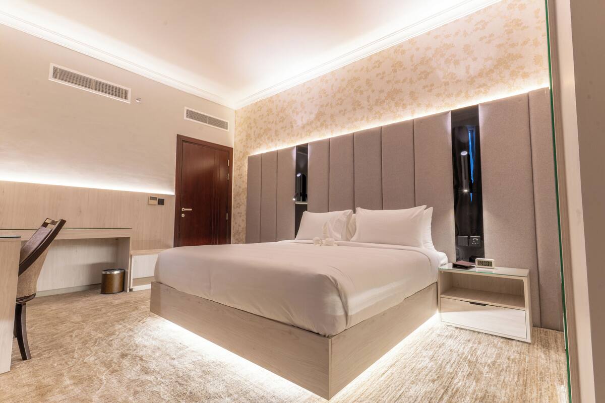 Una habitación de hotel moderna con una cama grande, un escritorio y una mesita de noche con un reloj.