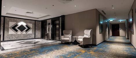 A hotel lobby with a marble wall, a patterned carpet, and two armchairs.