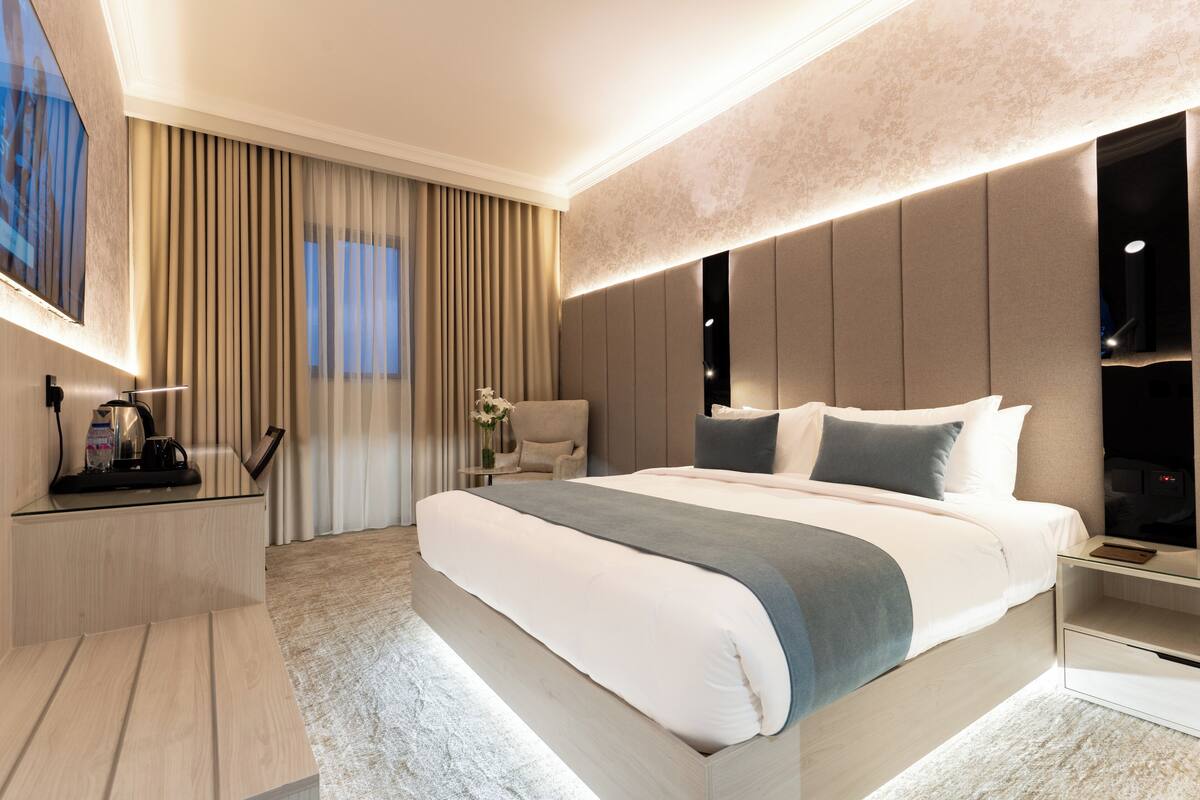 Una habitación de hotel moderna con una cama grande, una mesita de noche con lámpara, una silla y un televisor.