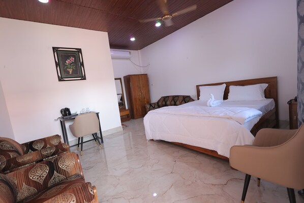 Habitación de hotel con cama, escritorio, sillón y ventilador de techo.